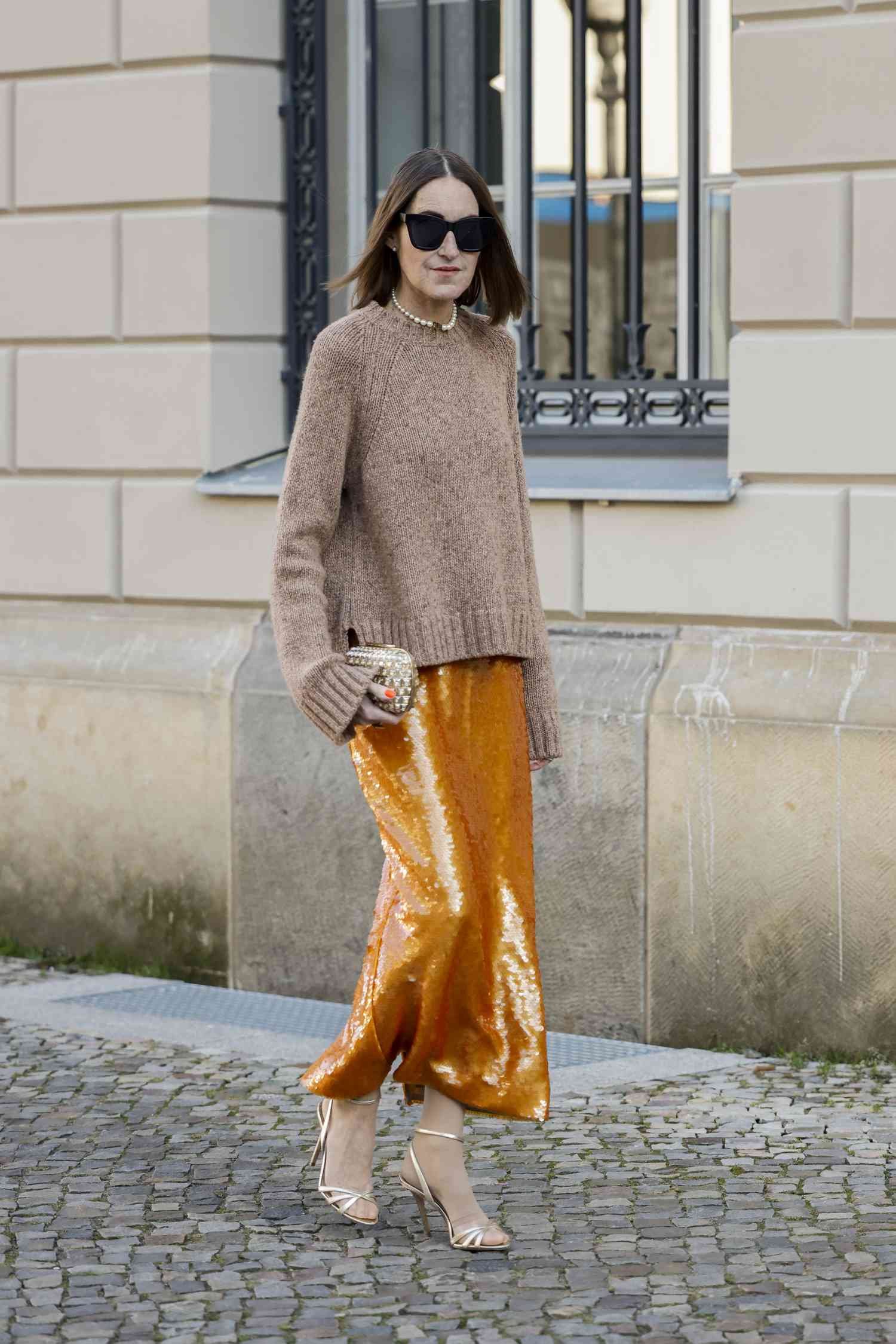 Person wearing a light brown sweater and orange sequined maxi skirt