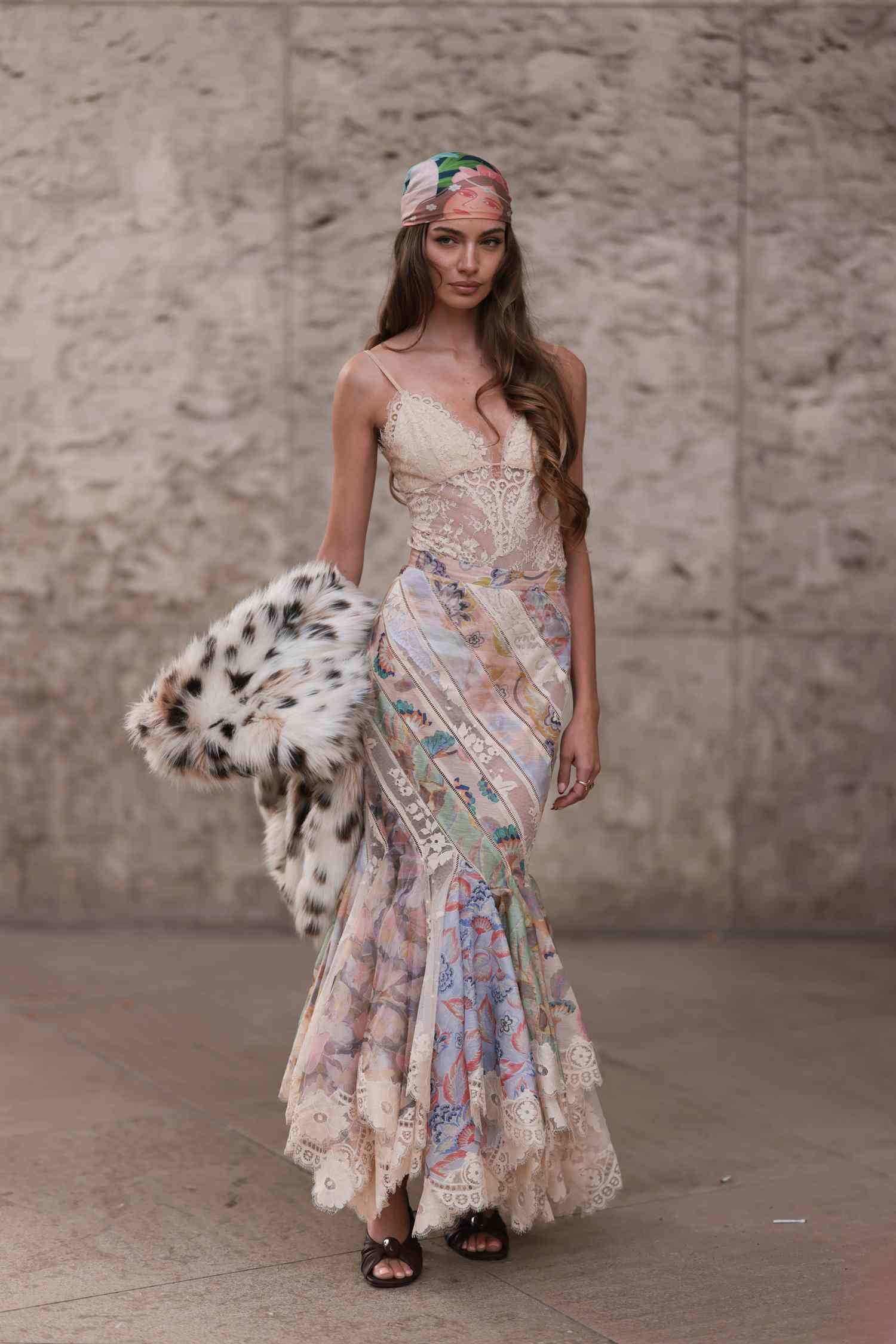 Mara Lafontan is seen wearing away colorful satin headscarf, a white lace top and a long colorful stripe satin skirt. The patterned skirt HA gathered ends. She also wear angstrom fur jacket in Leo during the Zimmermann show Womenswear Spring/Summer 2025 as part of capital of France Fashion Week