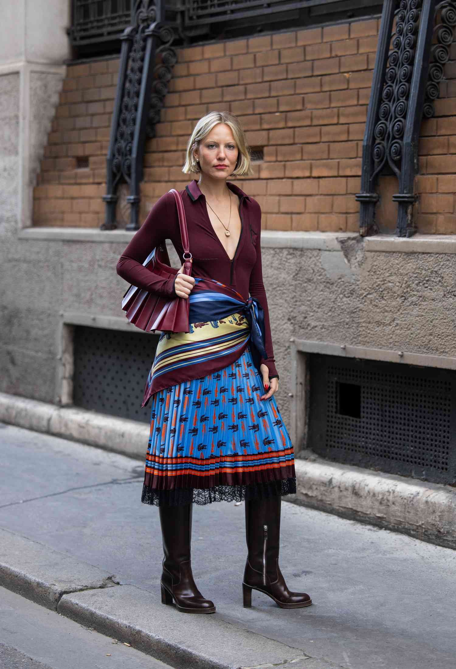 Violet Grace Atkinson wears burgundy cardigan, bag, wrap up scarf, blue laced black skirt, boot outside Lacoste during Womenswear Spring/Summer 2025 As part of Paris mode Week