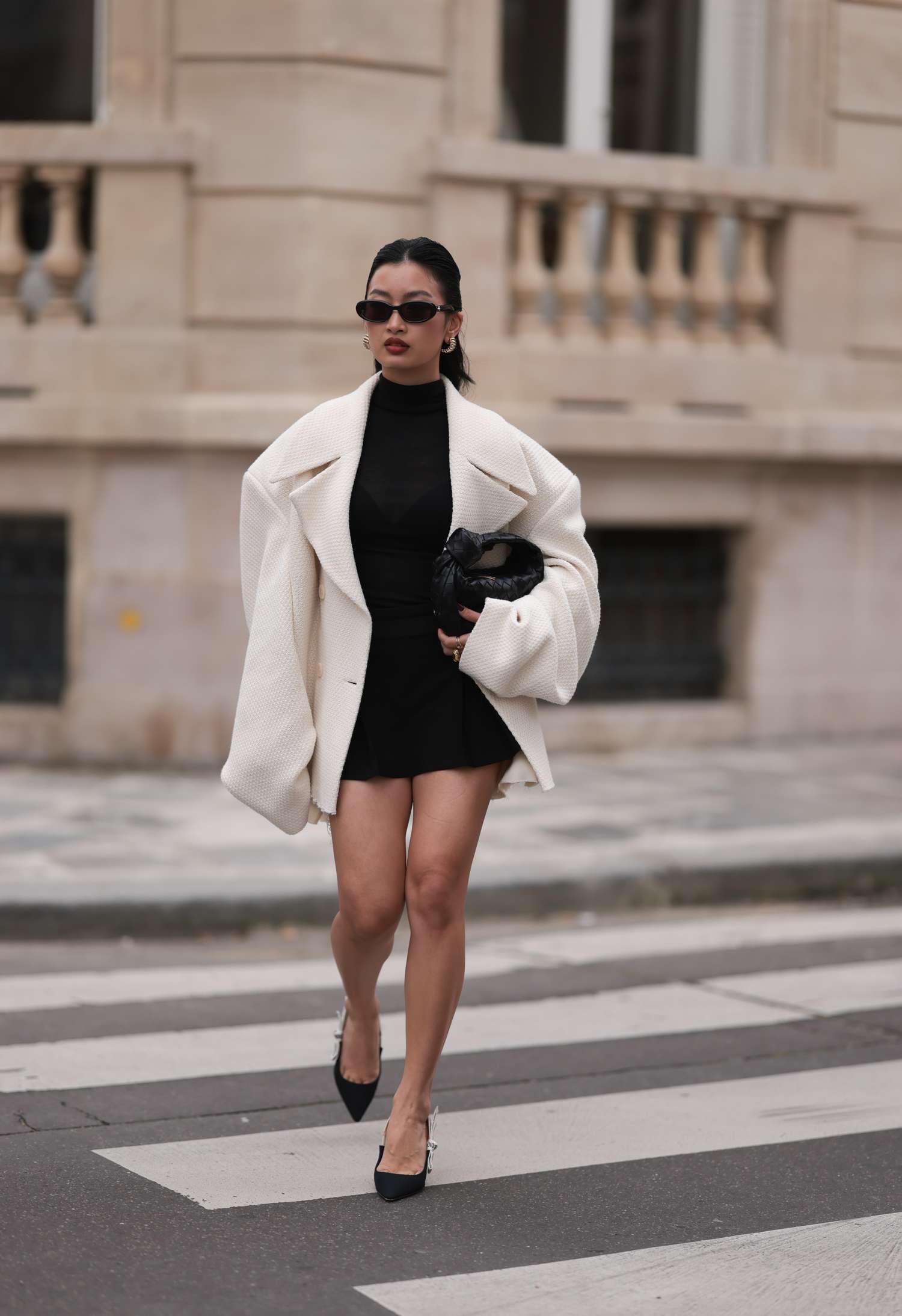 Thanya Wong see eroding Gentle monster black sunglasses, PolÃ¨ne City of Light gold jewellery / earrings, Vautrait cream Caucasian oversize woollen short coat / jacket, cos black high neck top, Bershka black short skirt, Bottega Veneta black woven leather Jodie small bag and Dior black logo heels, during Womenswear Spring/Summer 2025 as part of Paris mode Week on September 30, 2024 in Paris, France. 