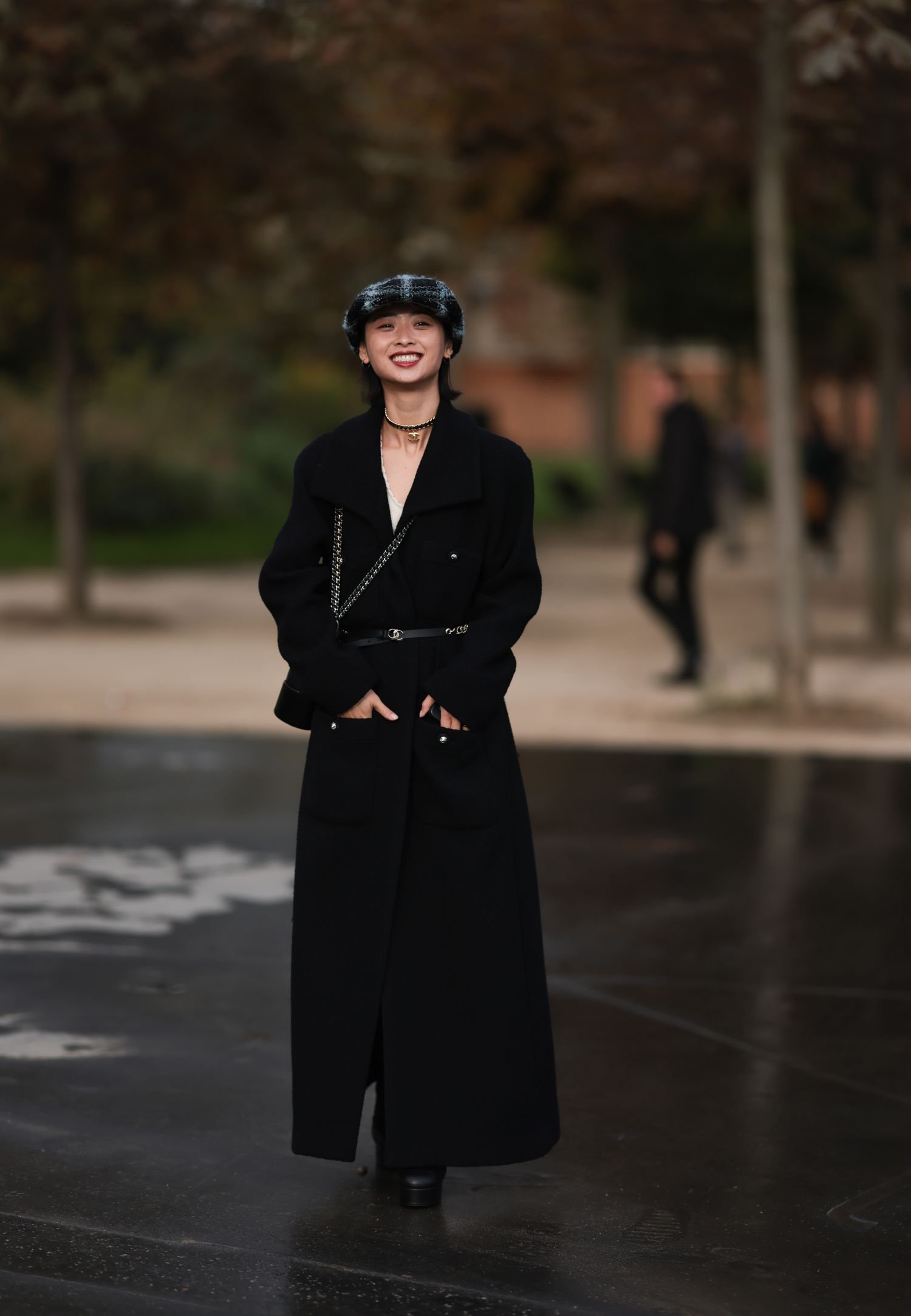 Yaqian Lan is seen wearing a black and blue tweed hat, A long blackness wool coat, A blackness Chanel belt and black boot with a black and gold Chanel necklace during the Chanel Show Womenswear Spring/Summer 2025 As part of Paris style hebdomad on Oct 01, 2024 in Paris, France.